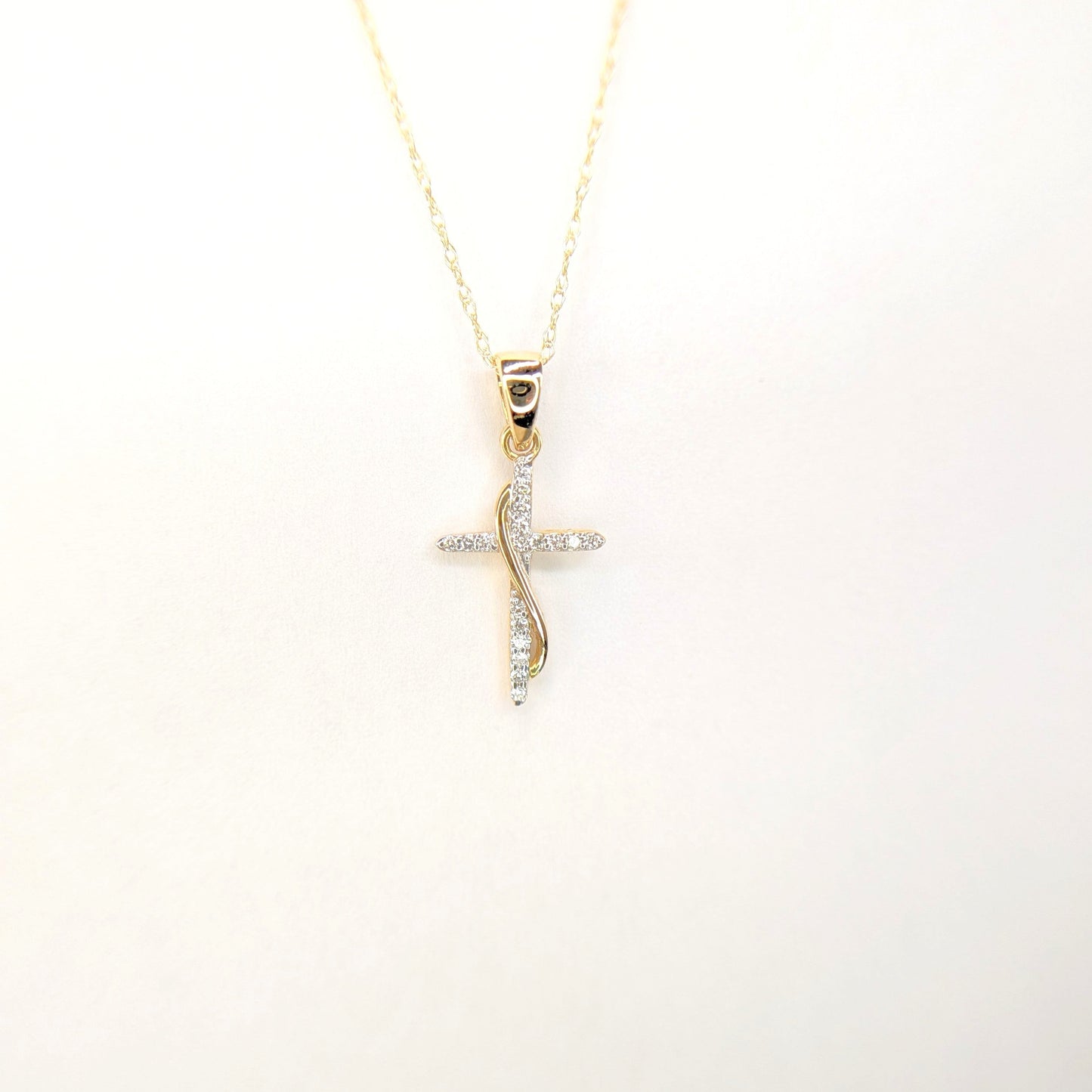 A gold chain displays a delicate diamond cross pendant against a soft white background.