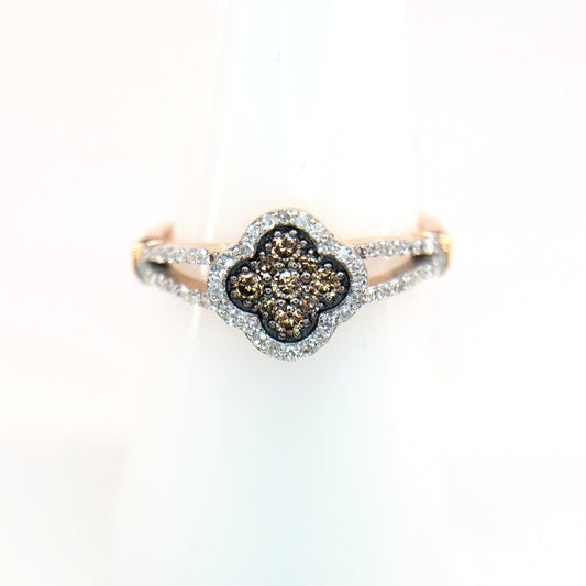 A rose gold ring with four-leaf clover. The center of the ring contains cognac diamond with an outer layer or white diamonds. The Ring sparkles on a white display stand.