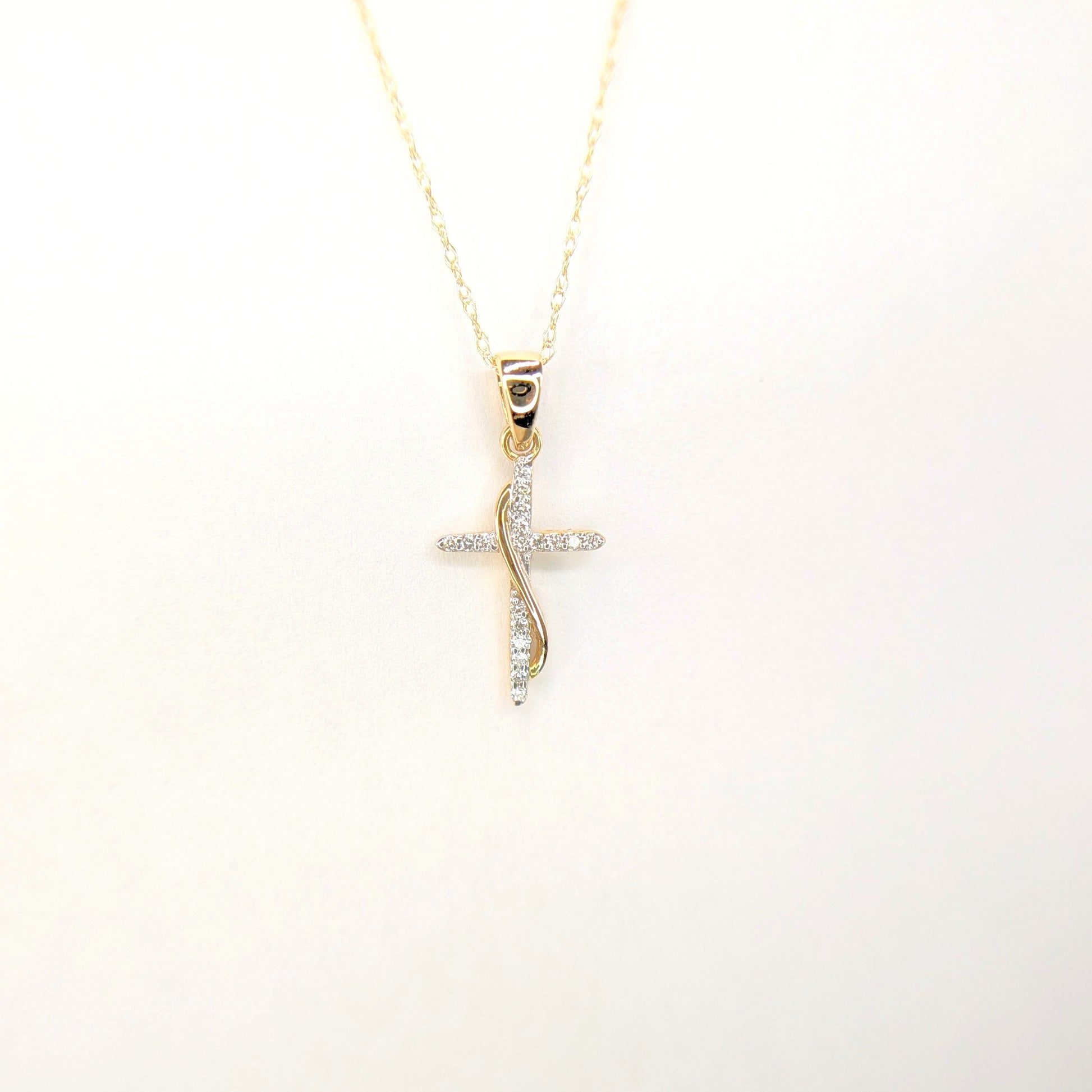 A gold chain displays a delicate diamond cross pendant against a soft white background.