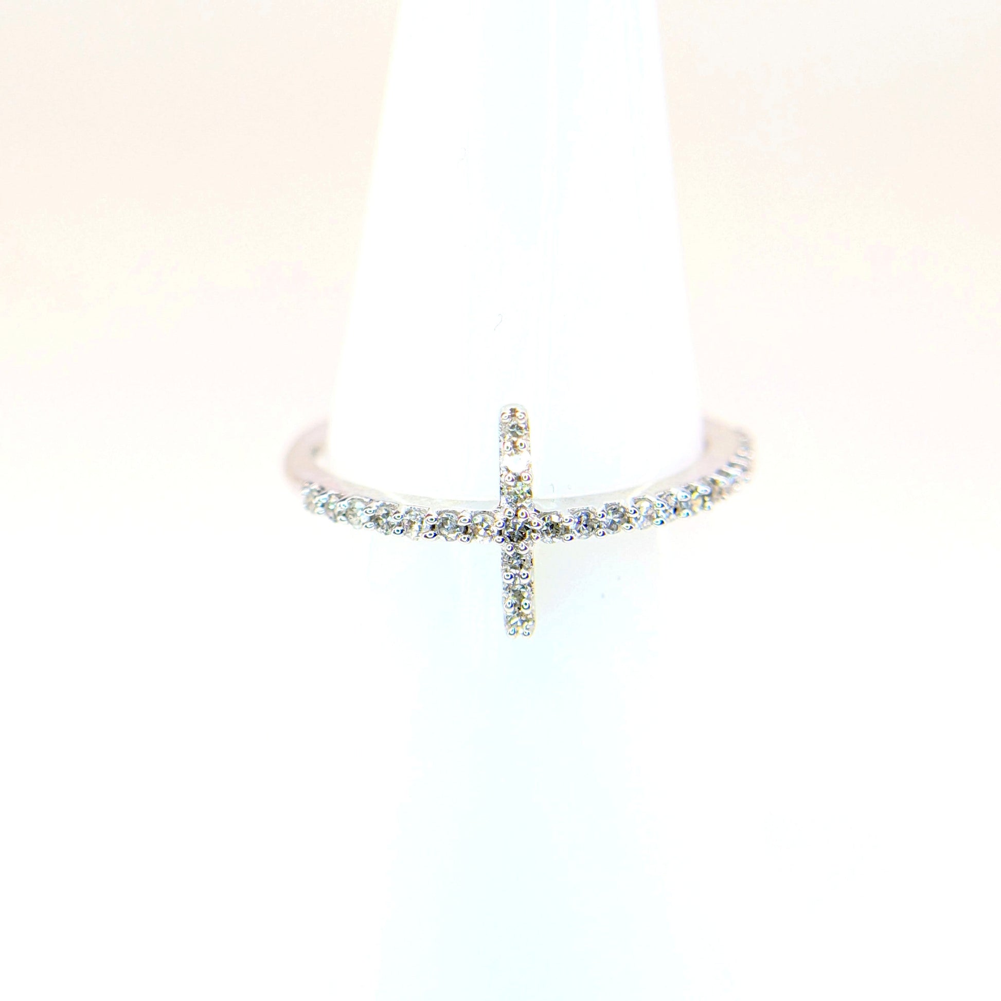 A white gold diamond cross ring sparkles atop a white display cone.