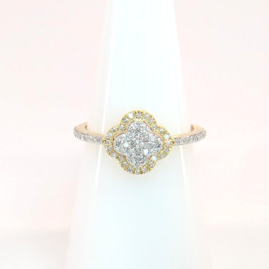 Close-up shows a sparkling diamond yellow gold ring featuring a clover design resting on a white display stand.